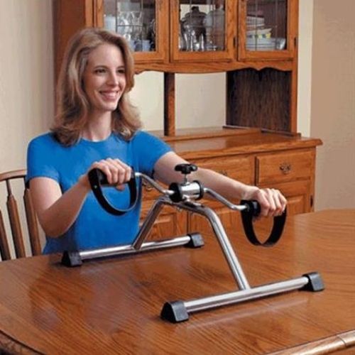 Pedal Exerciser In Use Image of woman seated at the table using the Pedal Exerciser.